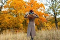 Fashionable young woman in an elegant long coat in a stylish hat stands among the dry grass and enjoys the autumn scenery in the Royalty Free Stock Photo