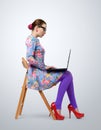 Fashionable young woman in glasses sitting on a chair with a laptop Royalty Free Stock Photo