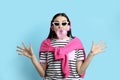 Fashionable young woman with headphones blowing bubblegum on light blue background Royalty Free Stock Photo