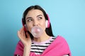 Fashionable young woman with headphones blowing bubblegum on light blue background Royalty Free Stock Photo