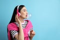 Fashionable young woman with headphones blowing bubblegum on light blue background, space for text Royalty Free Stock Photo