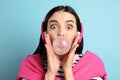 Fashionable young woman with headphones blowing bubblegum on light blue background Royalty Free Stock Photo