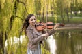 Fashionable young woman emotionally playing the violin in the park