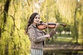 Fashionable young woman thoughtfully and dreamily plays the violin in the park