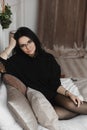 A fashionable young woman with perfect dark hair in an elegant black dress and round glasses posing on the bed Royalty Free Stock Photo