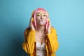 Fashionable woman in pink wig with headphones blowing bubblegum on yellow background Royalty Free Stock Photo