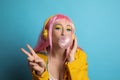 Fashionable young woman in pink wig with headphones blowing bubblegum on yellow background Royalty Free Stock Photo
