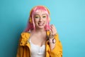 Fashionable young woman in pink wig with headphones chewing bubblegum on yellow background Royalty Free Stock Photo