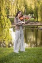 Fashionable young woman playing the violin in the park. The general plan