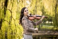 Fashionable young woman playing the violin in the park. The half-size portrait