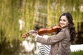 Fashionable young woman playing the violin in the park and smiles