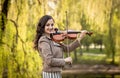 Fashionable young woman playing the violin in the park and smiles. The half-size portrait