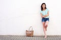 Fashionable young woman with purse leaning against white wall Royalty Free Stock Photo