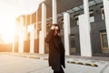 Fashionable young woman in stylish black blazer walks near building in city beautiful at sunset. Lovely gorgeous girl travels and Royalty Free Stock Photo