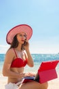 Fashionable young woman talking on mobile phone and using a tablet on the beach Royalty Free Stock Photo