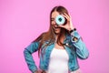 Fashionable young woman trendy in jeans wear covers eyes with sweet donut near vintage pink wall in the room. Studio creative Royalty Free Stock Photo