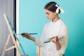 fashionable youth artist painting on easel with brush and palette