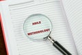 Fast changes concept. AGILE METHODOLOGY on a blank page of a business notebook through a magnifying glass Royalty Free Stock Photo