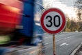 A fast driving blue speeding truck with motion blur effect near the traffic sign limiting the maximum speed to 30 kph