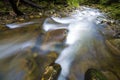 Fast flowing through wild green forest river with crystal clear smooth silky water falling from big wet stones in beautiful Royalty Free Stock Photo