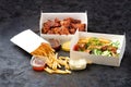 Fast food - box of crispy grilled chicken legs with Greek souvlaki and French fries on a dark stone surface with Royalty Free Stock Photo
