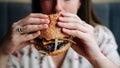 Fast food burger eat. Pretty Young Happy Woman Eating Tasty Hamburger. Junk Food Concept. Royalty Free Stock Photo