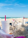 Fast food containers and drink cups on the beach with towels and sunbather. Blue sky and water with beach sand and a picnic. Trash Royalty Free Stock Photo