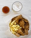 Fast food: fried chicken legs, spicy wings, French fries and chicken fingers in paper box, sauce and glass of cold beer over white