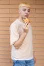 Enjoying a European blond man dressed in a beige T-shirt and jeans holding a burger in his hand Royalty Free Stock Photo