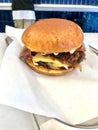 Fast Food Hamburger with Aioli Sauce, Cheddar Cheese, Mayonnaise and Bacon on White Burger Sheet / Street Food Cheeseburger Royalty Free Stock Photo