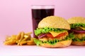 Fast food - juicy hamburger, french fries potatoes and cola drink on pink background. Take away meal. Unhealthy diet concept with Royalty Free Stock Photo