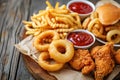 Fast food meals. Onion rings, french fries, chicken nuggets and fried chicken on wooden table
