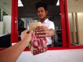 A fast food restaurant worker hands over an order of food to a customer at a drive thru counter.