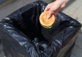 Fast food and unhealthy eating concept - hand throwing a burger in trash on street Royalty Free Stock Photo