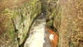 Fast full-flowing foamy water between sandstone rocks, orange sediments on dirty bank. Deep riverbed hewed into rock