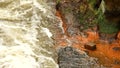 Fast full-flowing foamy water between sandstone rocks, orange sediments on dirty bank. Deep riverbed hewed into rock