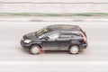 Fast moving black car on the city road. SUV in motion side view. Vehicle driving along the street in city with blurred background Royalty Free Stock Photo
