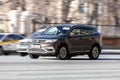 Fast moving Geely Atlas on the city road. Brown SUV front side view. Chinese auto in fast motion with blurred background. Speeding