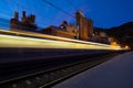 Fast-moving light of a train on a railway with urban architecture in the background Royalty Free Stock Photo