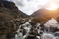 Fast moving river flowing over boulders with distant mountains and bright sunlight