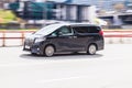 Fast moving Toyota Alphard on the city road. Black van rides on street. Commercial auto in fast motion with blurred background.