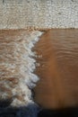 fast moving whitewater and brown water over a small weir with river back made of brick