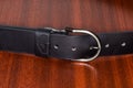 Fastened leather belt with semicircular frame buckle on wooden table