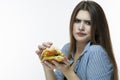 Fastfood Eating Concept. Young Caucasian Female Eating Burger With Displeasing facial Expression in Studio. Posing in Striped