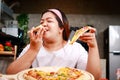 Fat Asian happy woman eating pizza, she holds two slices of pizza and eats deliciously in the kitchen at home. Royalty Free Stock Photo