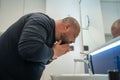 Fat, bald, bearded middle-aged man washes face in bathroom home int sink. Overweight and sweat