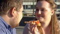 Fat boyfriend and girlfriend eating pizza outdoors romantic date, junk food diet Royalty Free Stock Photo