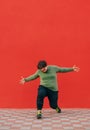 Fat curly young man in stylish street clothes dancing hip hop on a red wall background. Vertical Royalty Free Stock Photo