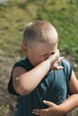 Fat dirty boy covers his face from spray. A child with blond hair and a dirty adult t-shirt. Unsanitary conditions. Street games o Royalty Free Stock Photo