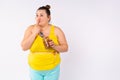 Fat dreamy overweight woman eats chocolate cream at night, looking side, smiling. Grey background and colorful pajamas